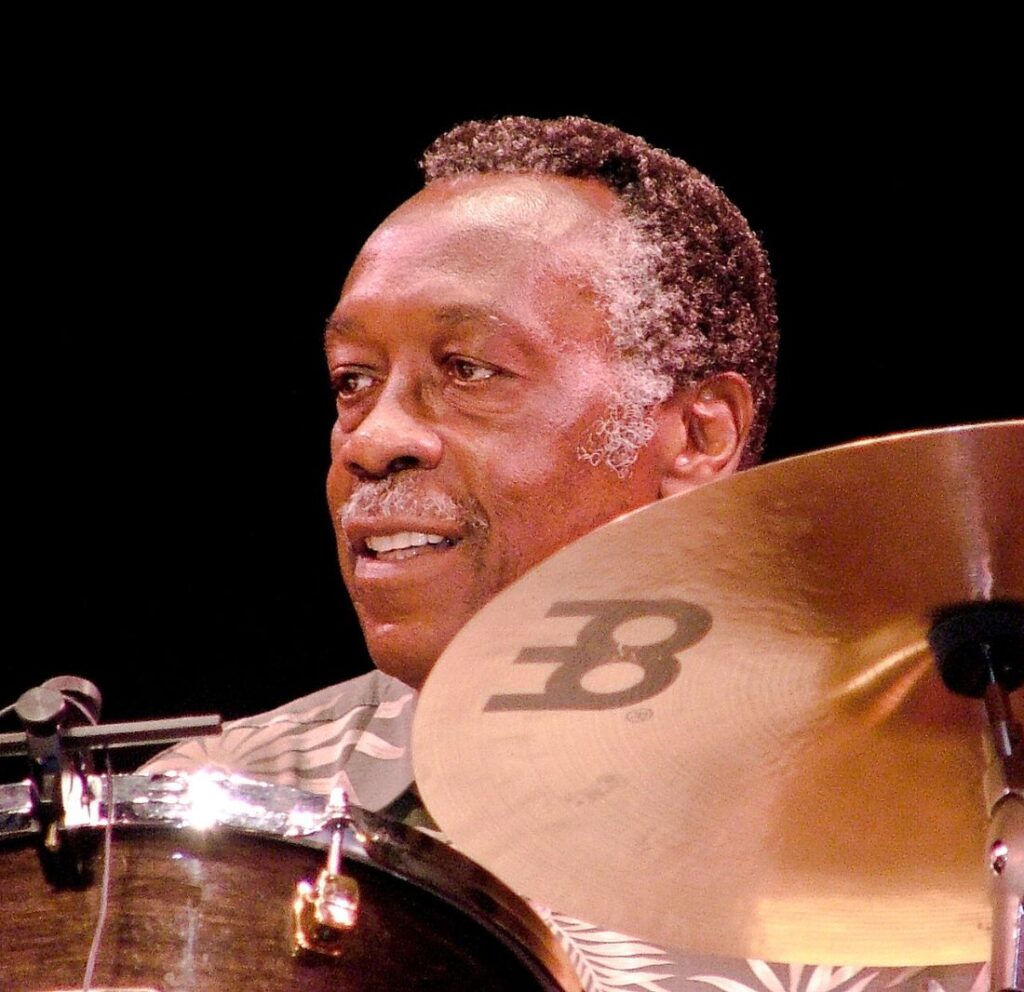 Clyde Stubblefield seated behind a drum kit mid-performance, a ride cymbal in the foreground