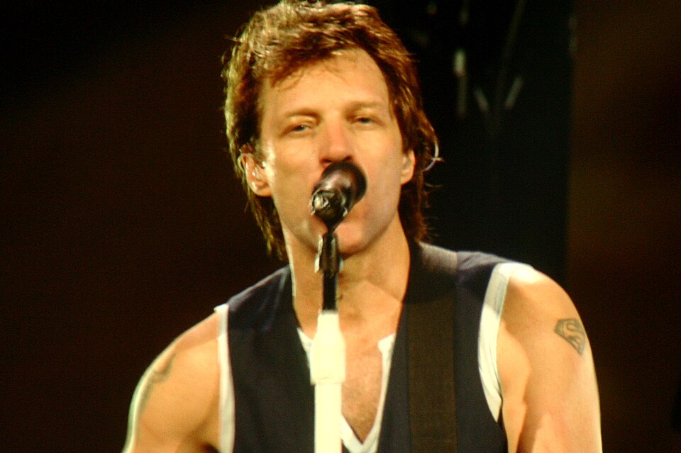 Jon Bon Jovi singing into a microphone on stage in a sleeveless vest