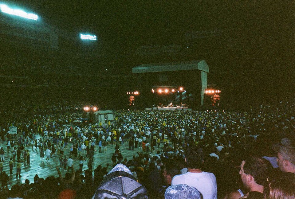 A huge crowd in the rain facing Bruce Springsteen on stage at Giants Stadium, with his face on the video screens